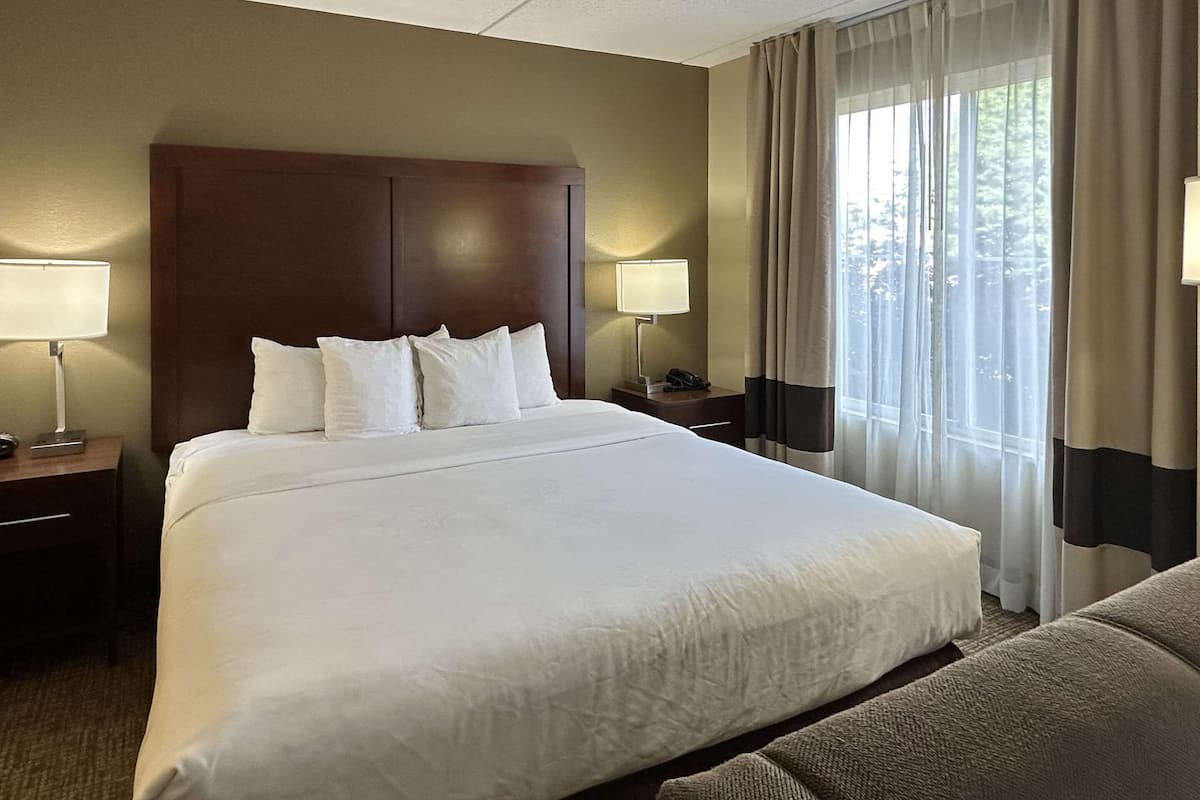 A hotel room with a large bed, two bedside tables with lamps, a wooden headboard, and a window with curtains.