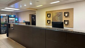 A hotel reception area with a dark reception desk, a wall-mounted clock, and an ATM machine. - Charlotte Suites (Charlotte)