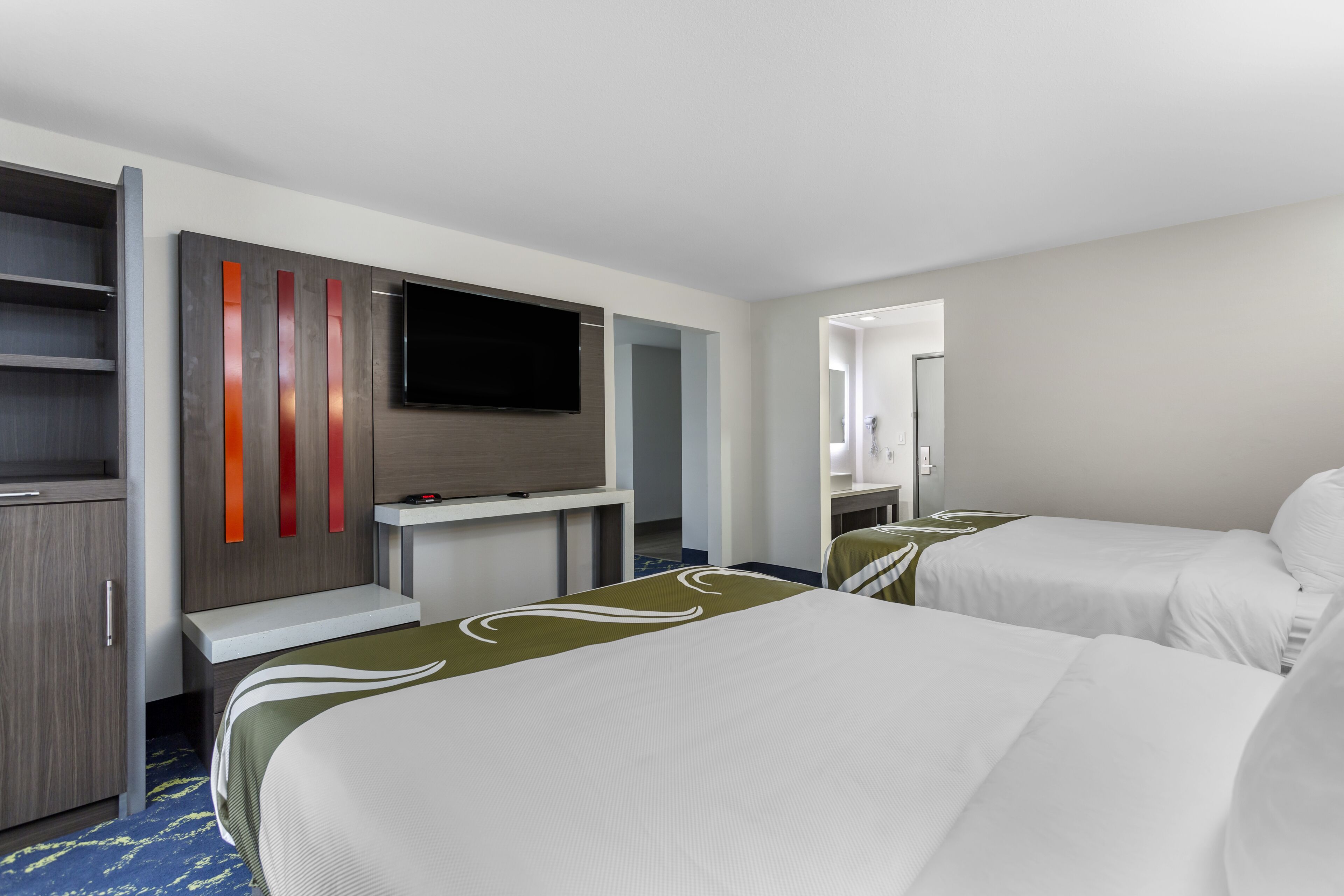 Ett hotellrum med två sängar, en platt-TV, en minibar och en spegel.
