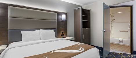 A hotel room with a large bed, a wardrobe, a bathroom with a shower, and a nightstand.