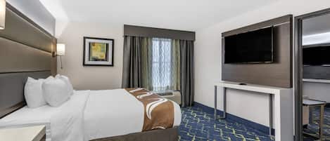 A hotel room with a large bed, a flat-screen TV, a desk, and a window with curtains.