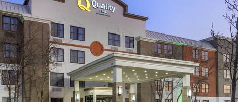 Un hotel con un llamativo letrero que dice "Quality Inn by Choice Hotels", una entrada cubierta y un área de estacionamiento.