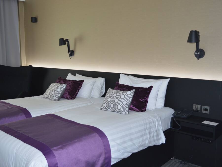 A hotel room with a large bed, two bedside tables, a phone, and a lamp on the wall.