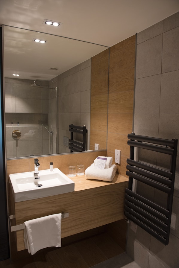 A modern bathroom with a large mirror, a sink, a towel rack, and a shower area.