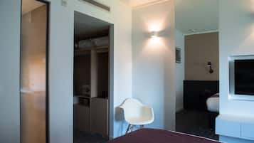 A hotel room with a bed, a white chair, a wardrobe, and a mirror.