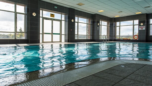 An indoor swimming pool with large windows, a lifeguard chair, and a shallow end sign. - Golden Jubilee Hotel (Clydebank)