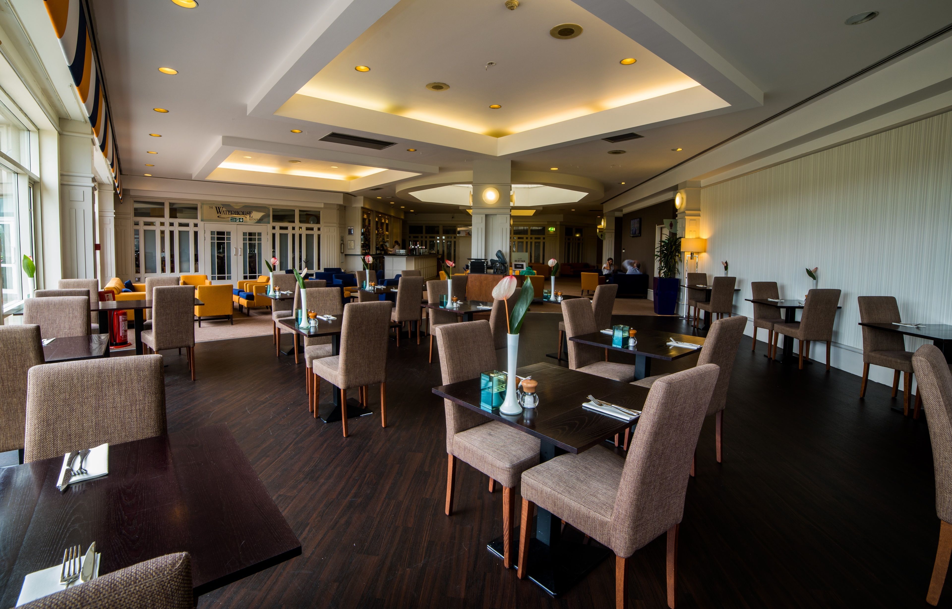 Eine großzügige Hotelhalle mit mehreren Gastronomiebereichen, einer Bar und einer Rezeption.