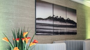 A modern interior with a sectional sofa, a large wall-mounted artwork depicting a mountainous landscape, and a potted plant with orange flowers. - Golden Jubilee Hotel (Clydebank)
