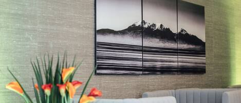 Un interior moderno con un sofá seccional, una gran obra de arte colgada en la pared que representa un paisaje montañoso y una planta en maceta con flores naranjas.