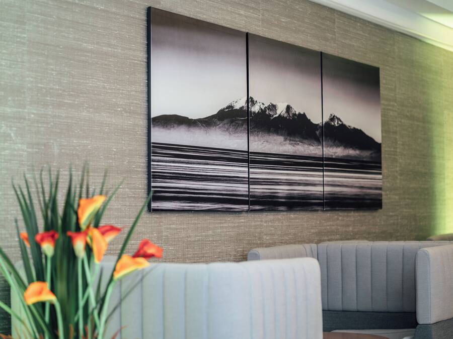 A modern interior with a sectional sofa, a large wall-mounted artwork depicting a mountainous landscape, and a potted plant with orange flowers.