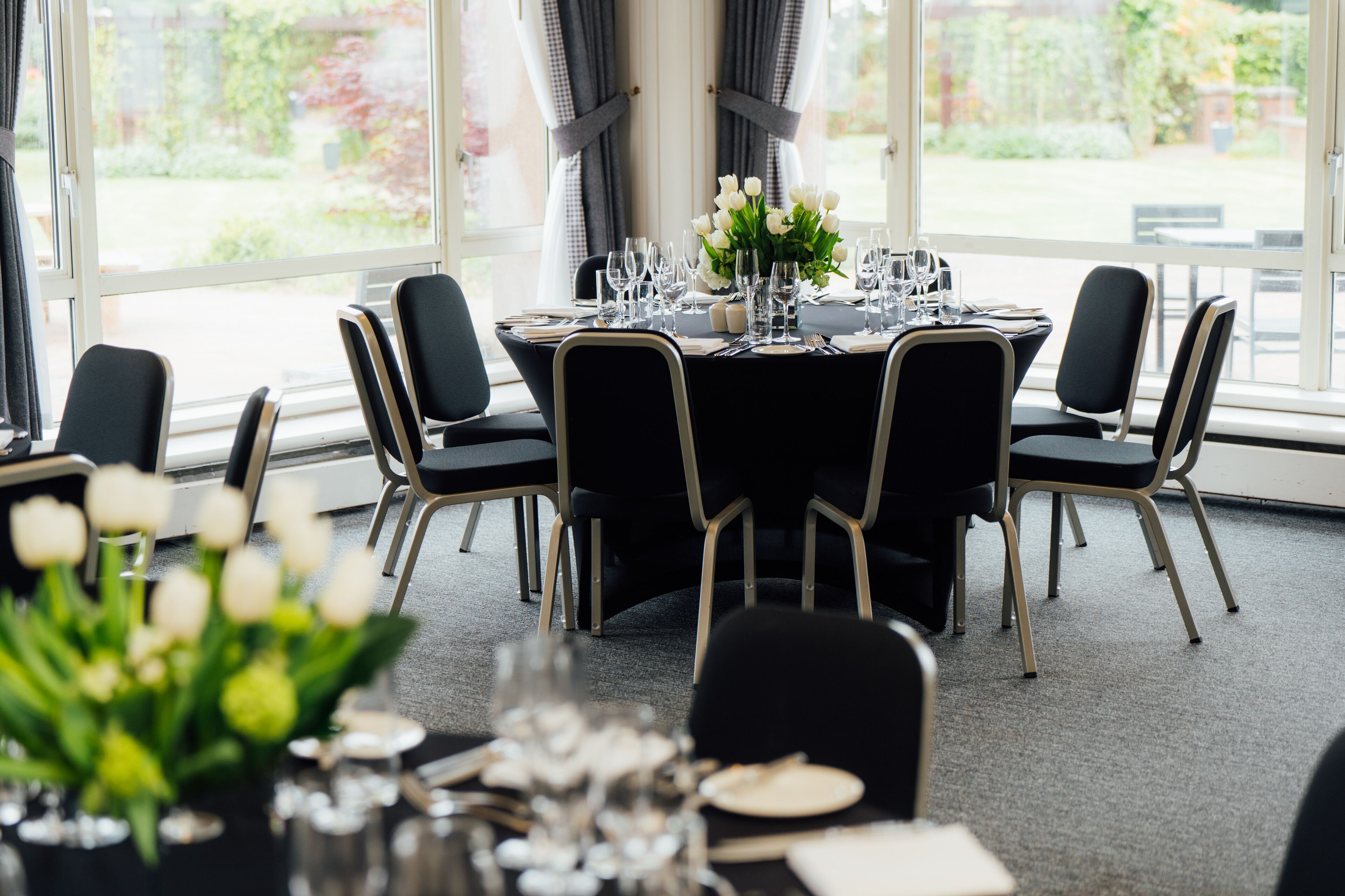 A dining area with a round table set for six, surrounded by black chairs with wooden legs.
