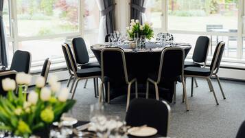 A dining area with a round table set for six, surrounded by black chairs with wooden legs.
