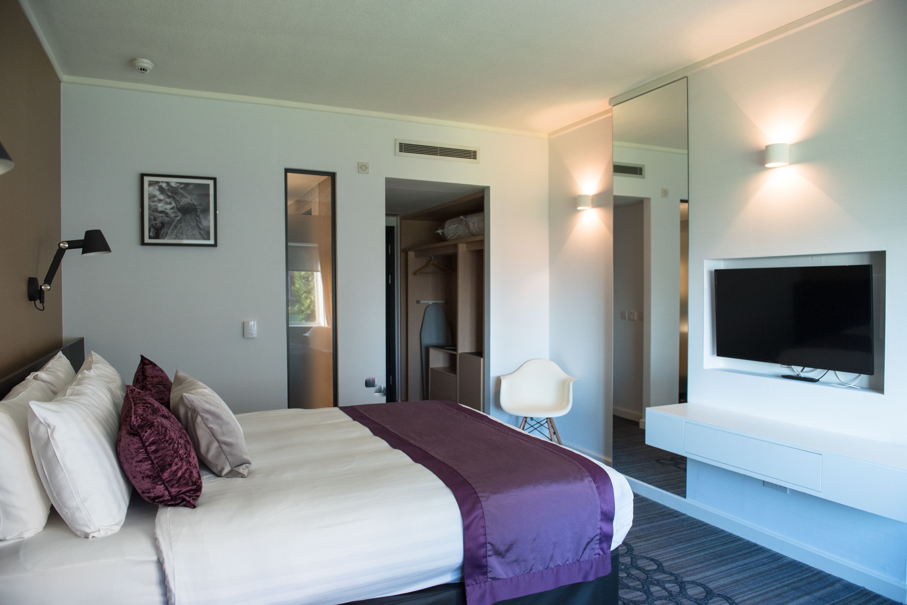 A hotel room with a bed, a TV, a desk, and a mirror.