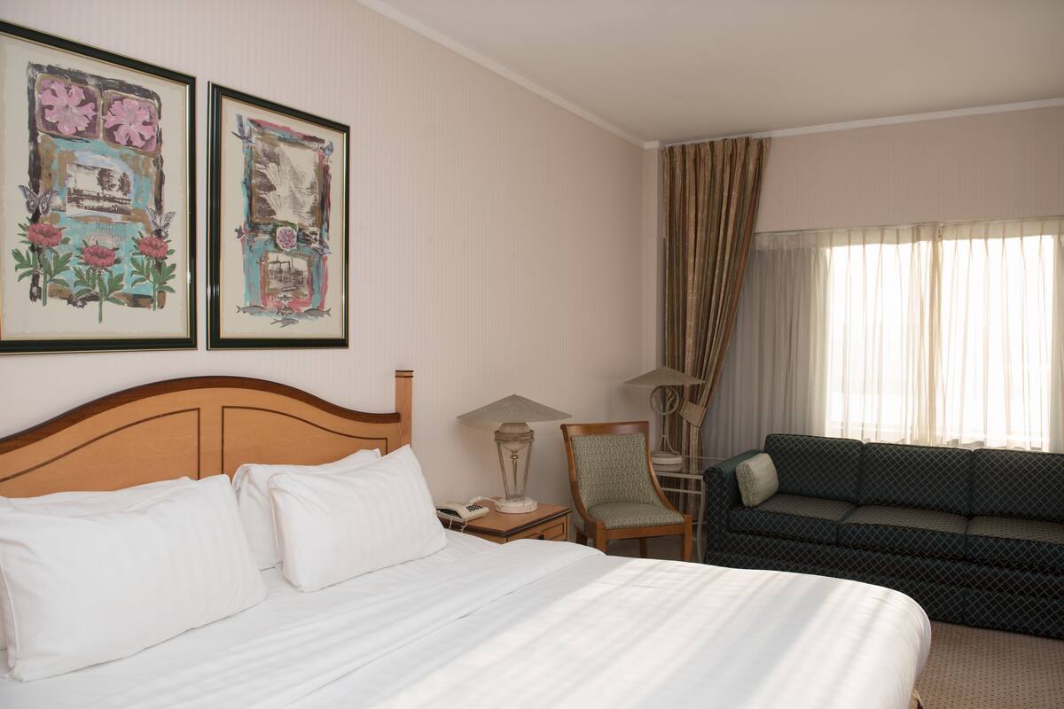 Una habitación de hotel con una cama, una silla, un sofá y dos cuadros en la pared.
