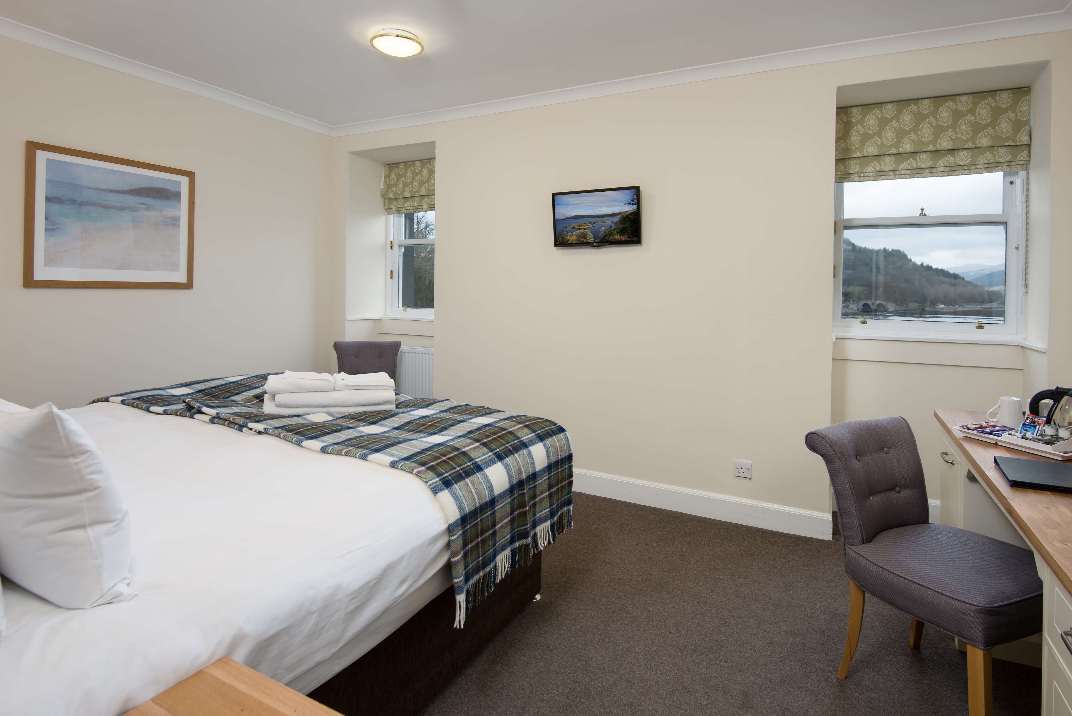 A bedroom with a bed, a chair, a desk, and two windows.