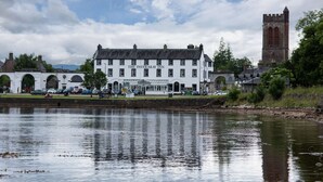 Un bâtiment blanc avec une enseigne indiquant « The Inveraray Inn », situé au bord d’un plan d’eau, avec une tour en arrière-plan.