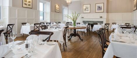A dining area with multiple tables set for service, wooden flooring, and chandeliers.