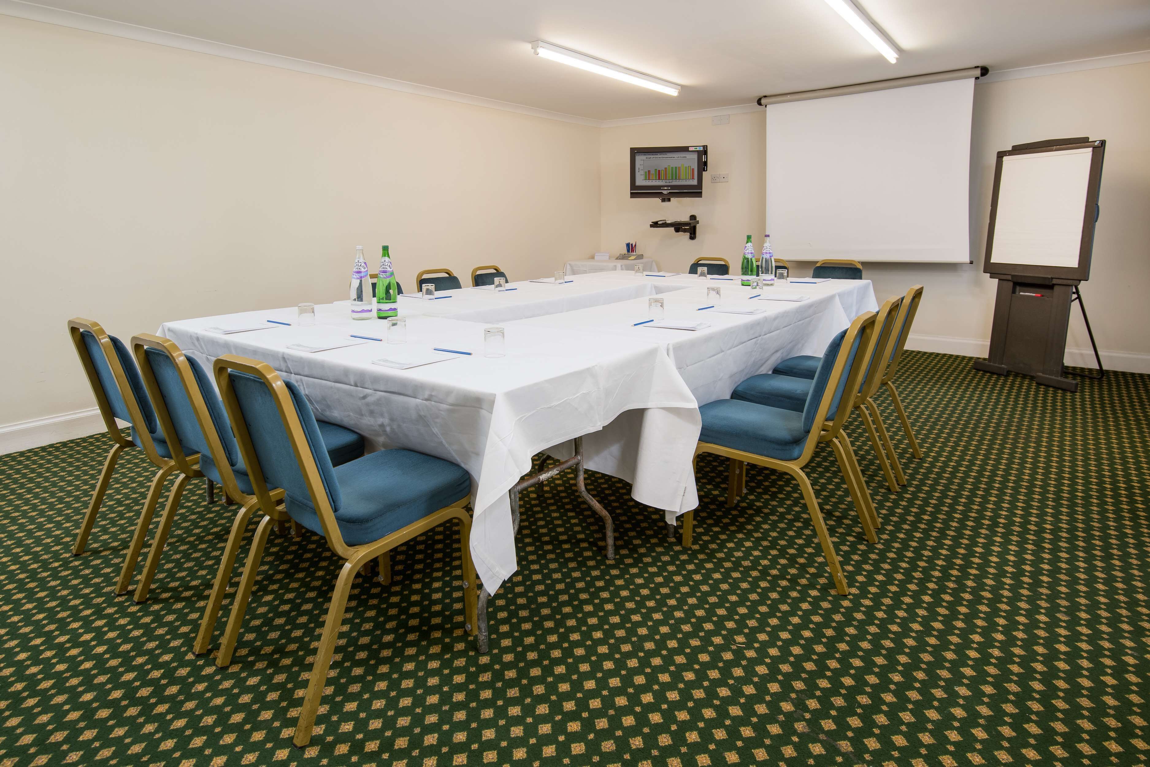 A conference room with a long table, blue chairs, and a projector screen.