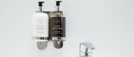 Two bottles of Silver Buckthorn hand wash soap mounted on a wall next to a chrome faucet.