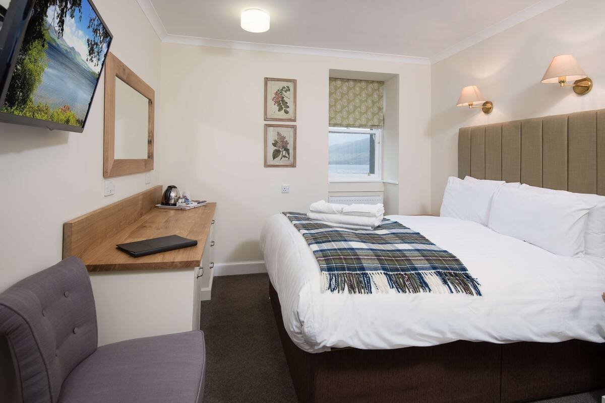 A hotel room with a bed, a desk, a chair, a television, and a window with a view.