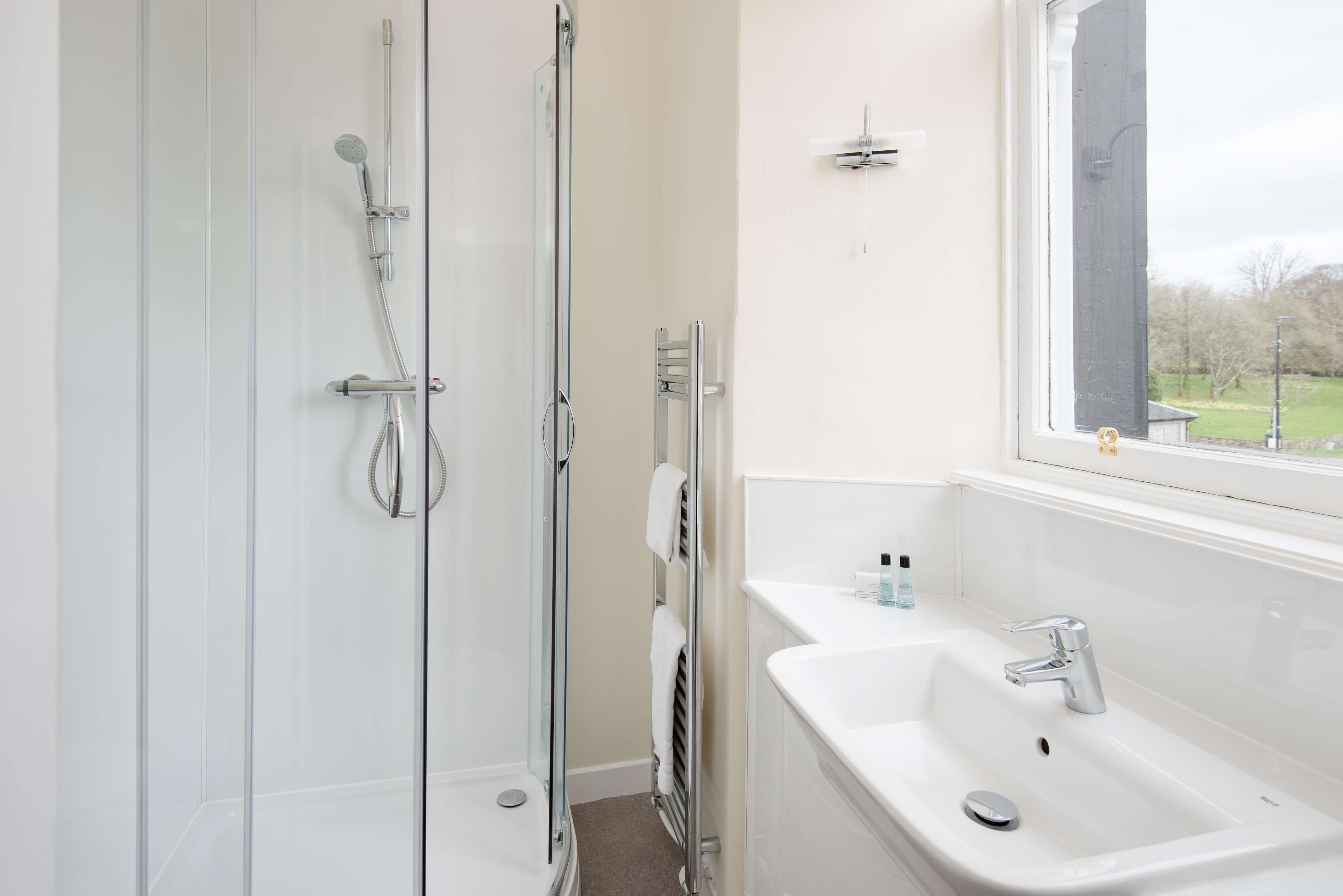 A modern bathroom with a glass-enclosed shower, a white sink, and a window with a view of the outdoors.