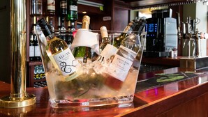 Un espace bar avec un présentoir en verre contenant des bouteilles de vin et de champagne.