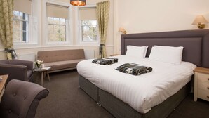 Une chambre à coucher bien aménagée, avec un grand lit, un canapé, une petite table avec une lampe et une fenêtre avec des rideaux.
