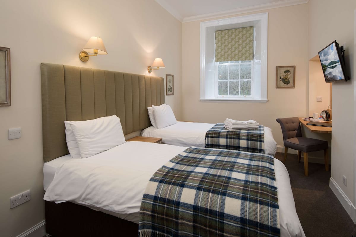 A hotel room with two beds, a desk, and a television.