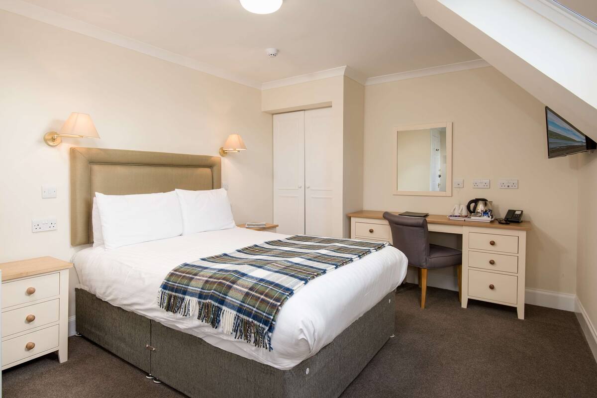 A hotel room with a bed, bedside tables, a desk, and a chair.
