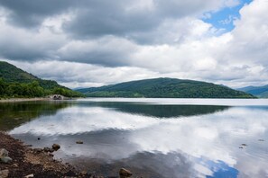 A calm lake with a bridge in the distance, surrounded by green hills and a cloudy sky.