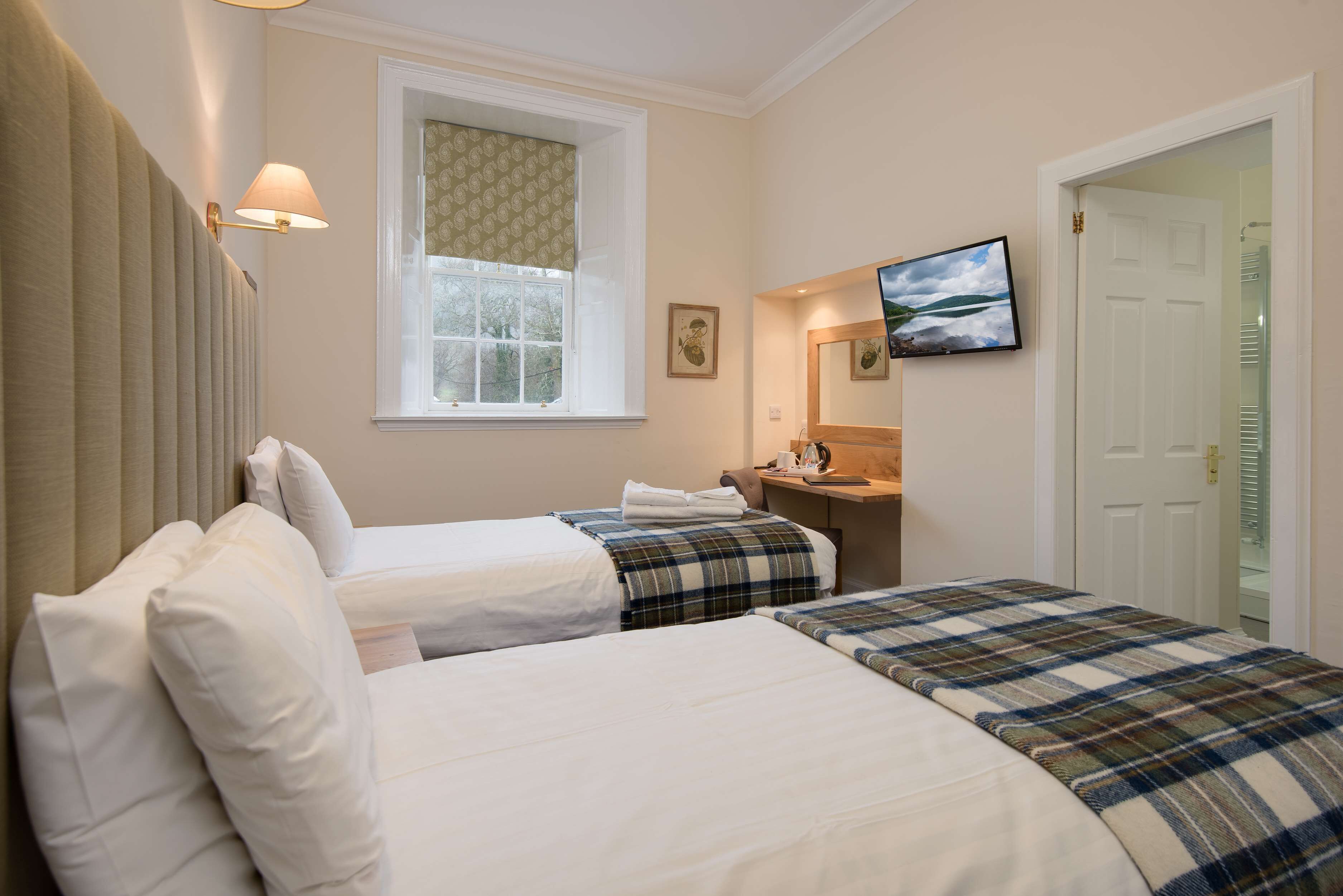 A hotel room with two beds, a window with a patterned curtain, a television on the wall, and a door leading to a closet.