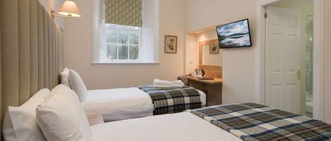 Habitación de hotel con dos camas, una ventana con cortina estampada, un televisor en la pared y una puerta que da a un armario.