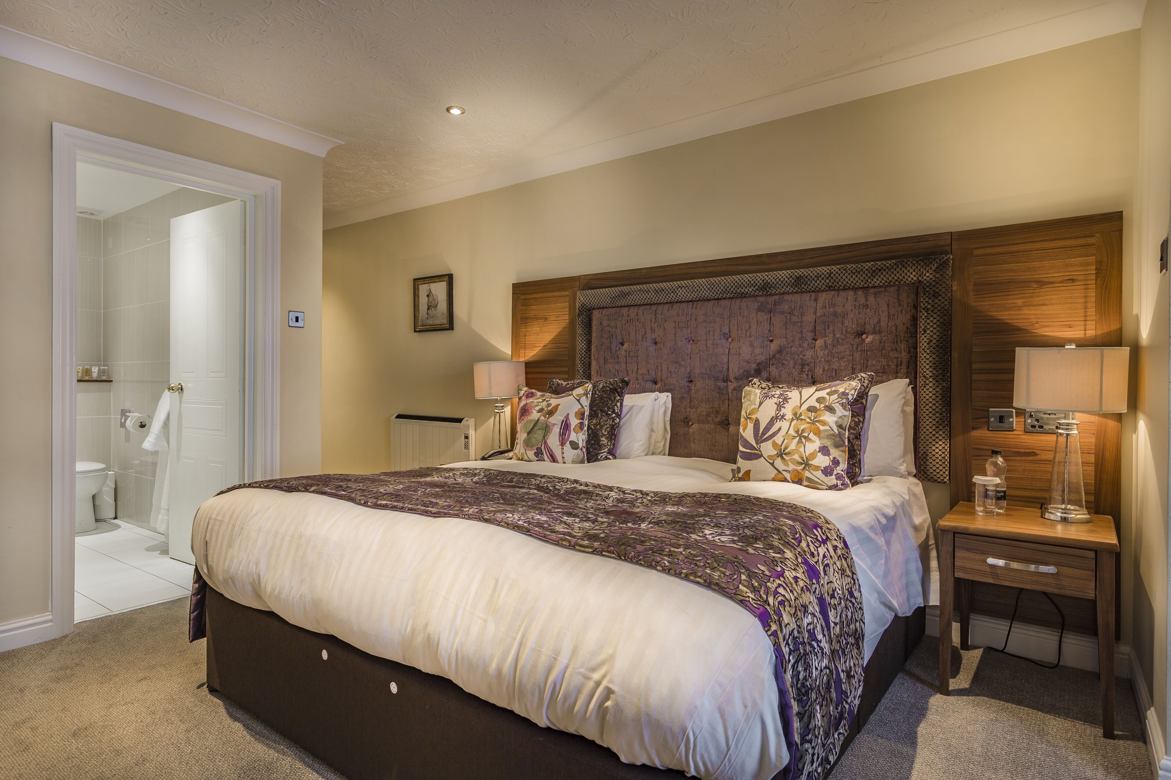 A well-lit bedroom with a large bed, bedside lamps, and a wooden headboard.