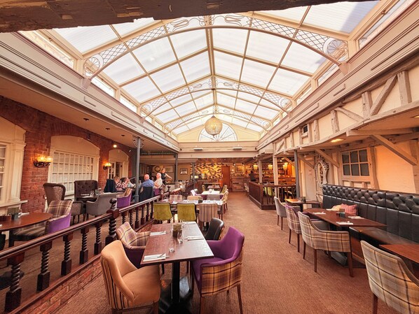 An indoor dining area with a high ceiling and glass panels, featuring tables and chairs, wooden beams, and a bar area. - The Admiral Rodney Hotel, Horncastle, Lincolnshire (Horncastle)