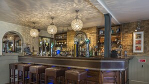 A bar area with a wooden counter, multiple stools, and a variety of bottles and glasses. - The Admiral Rodney Hotel, Horncastle, Lincolnshire (Horncastle)