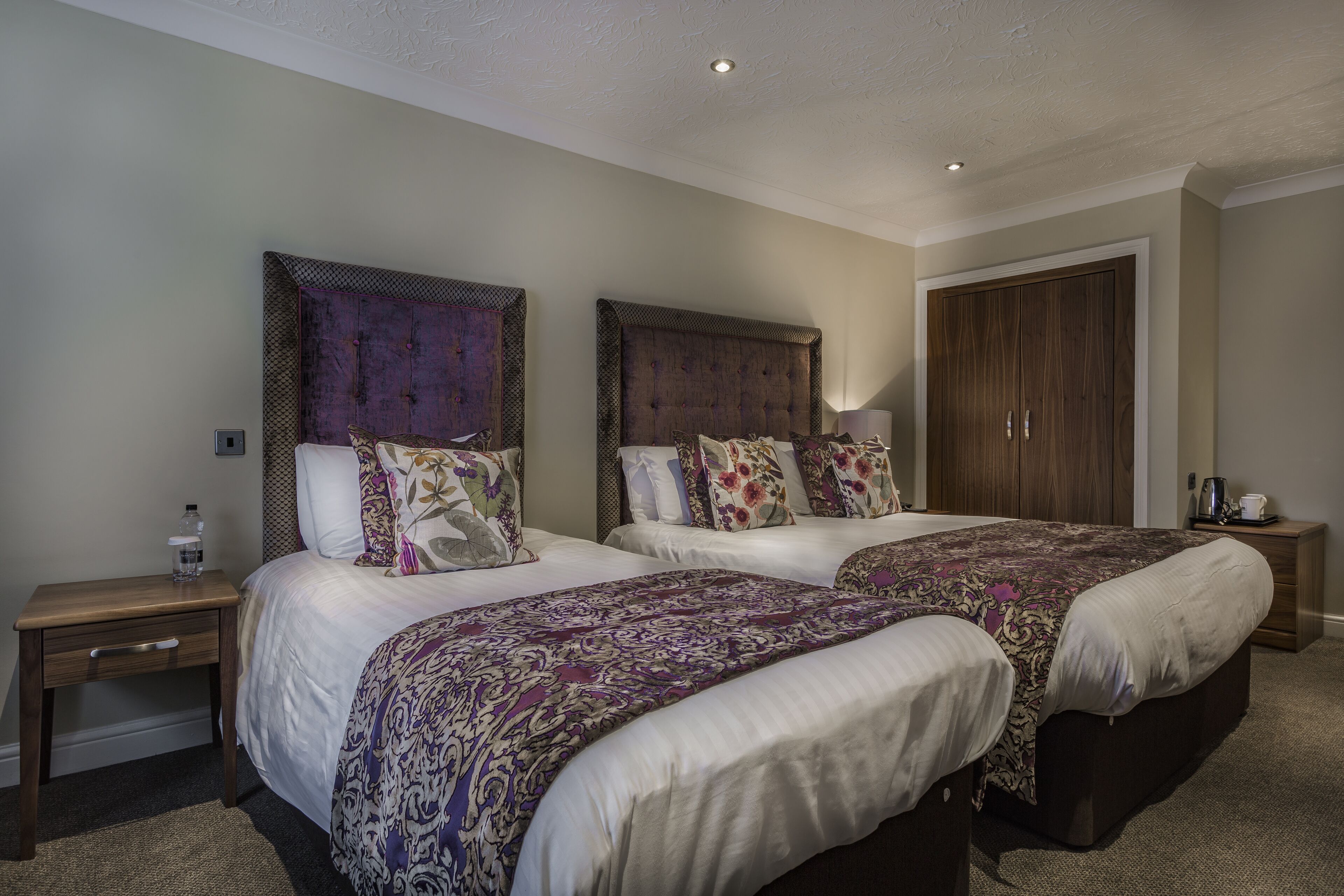 Une chambre d’hôtel avec deux lits, une armoire, une table de chevet et une lampe.