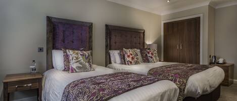 A hotel room with two beds, a wardrobe, a nightstand, and a lamp.