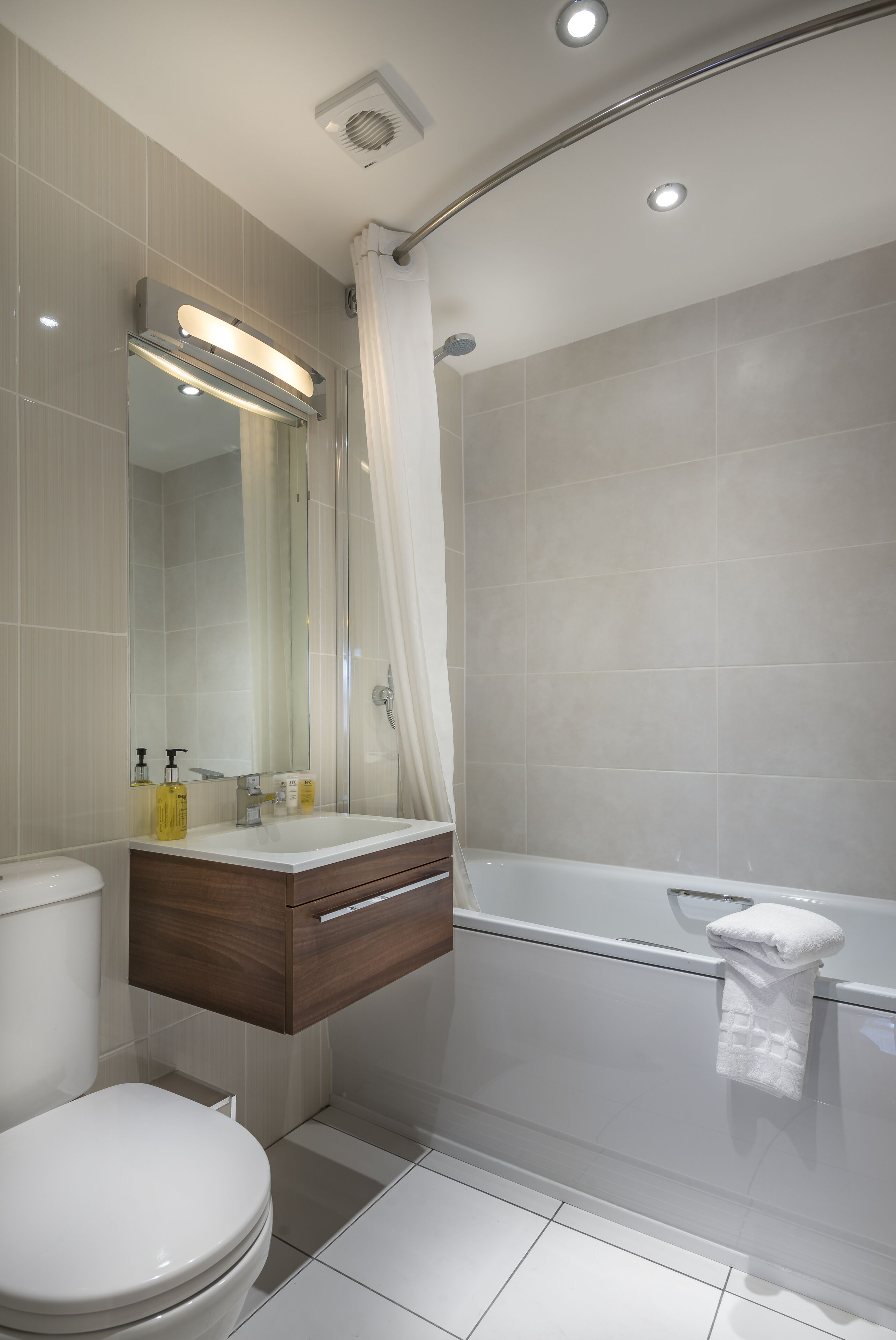 A modern bathroom with a toilet, vanity, mirror, and bathtub.