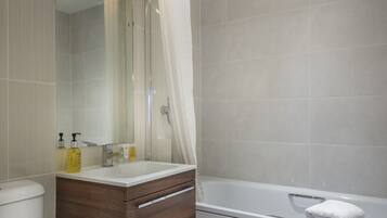 A modern bathroom with a toilet, vanity, mirror, and bathtub.