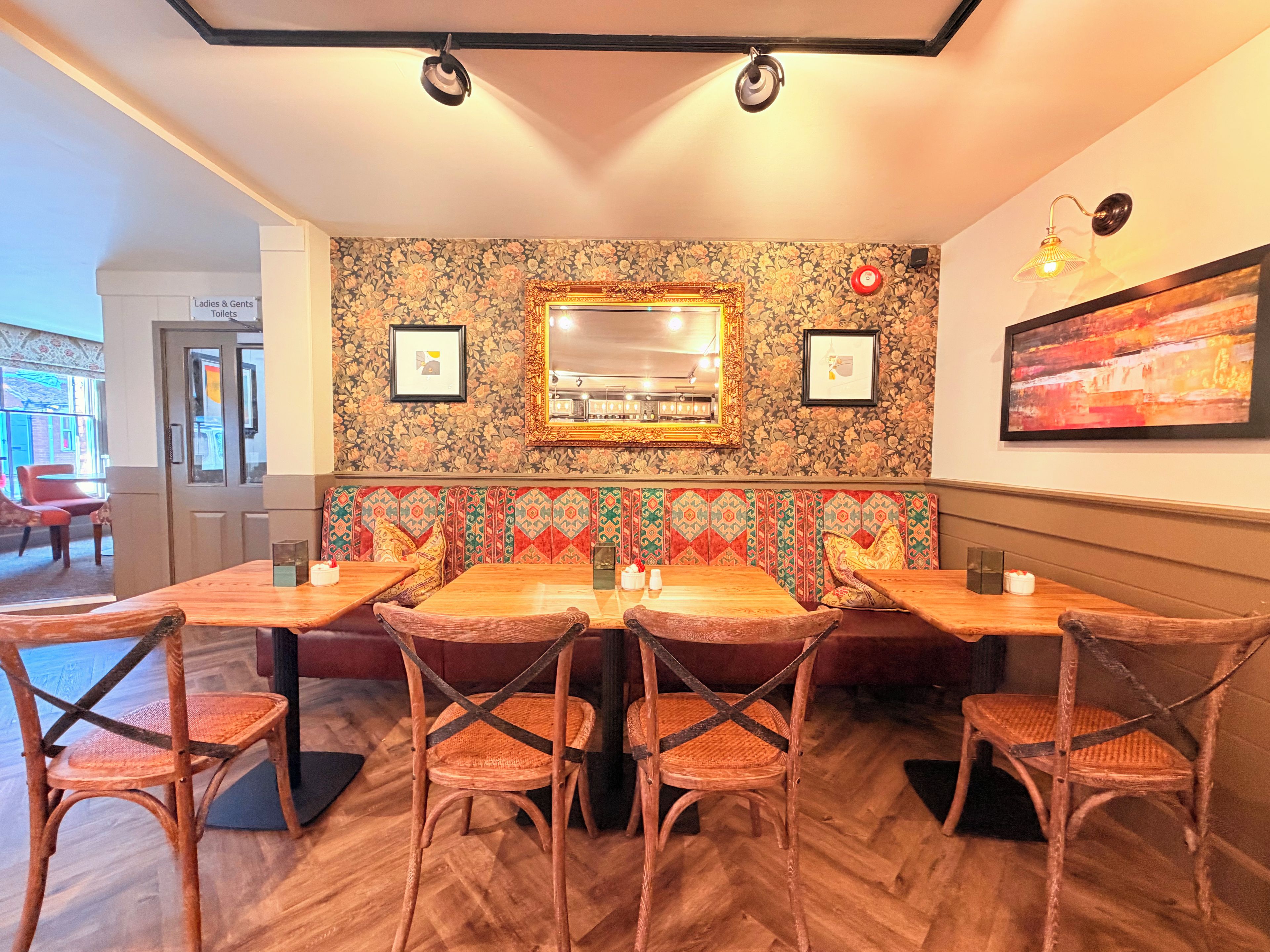 Un restaurant avec une table et des chaises en bois, un mur décoré de motifs floraux et un miroir.