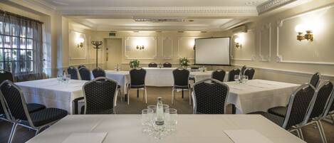 A conference room with round tables, chairs, and a projector screen.
