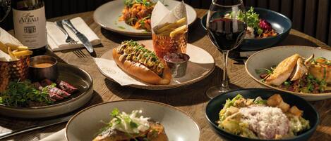 Una mesa de comedor con diversos platos, una botella de vino y una copa de vino tinto.