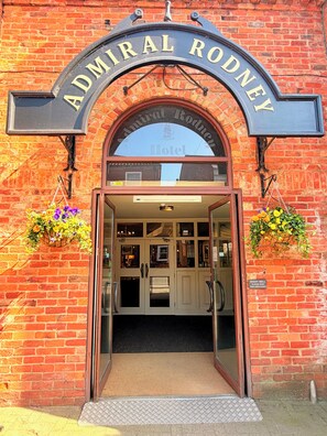 The entrance to the Admiral Rodney Hotel with a brick facade, a sign above the entrance, and flower baskets on either side. - The Admiral Rodney Hotel, Horncastle, Lincolnshire (Horncastle)