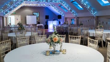 A banquet hall with round tables, chairs, and a central floral arrangement.