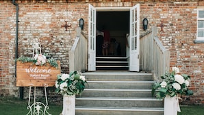 A rustic brick building with a wooden welcome sign, a staircase, and two flower arrangements. - The Admiral Rodney Hotel, Horncastle, Lincolnshire (Horncastle)