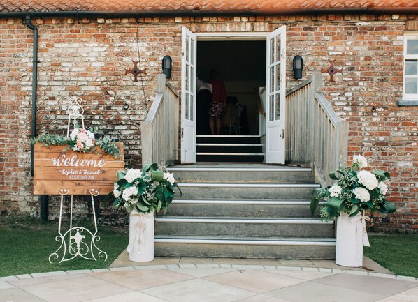 A rustic brick building with a wooden welcome sign, a staircase, and two flower arrangements. - The Admiral Rodney Hotel, Horncastle, Lincolnshire (Horncastle)
