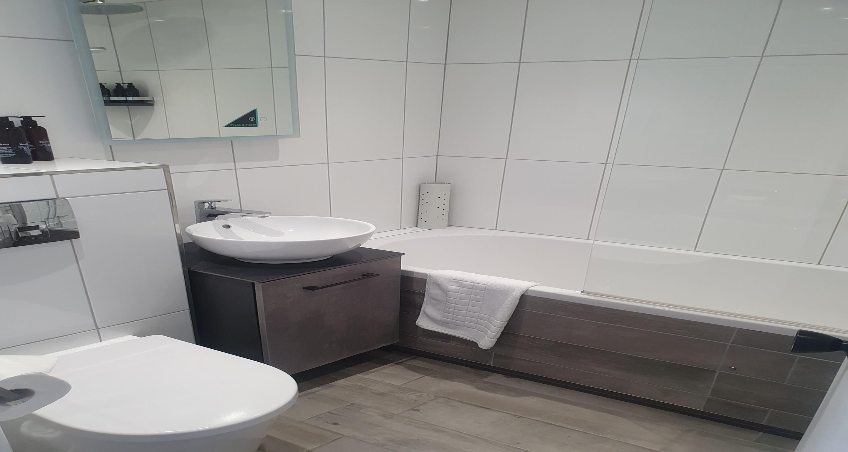Ein modernes Badezimmer mit Waschbecken, Toilette und Badewanne, alles in Weiß.