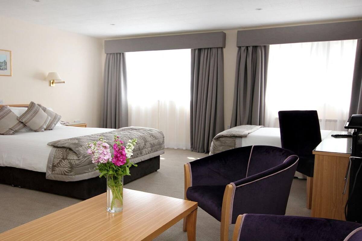 Une chambre d’hôtel avec un lit, un bureau, une chaise, un vase avec des fleurs et un tableau au mur.