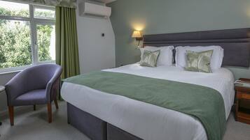 Ein Hotelzimmer mit einem Bett, einem Sessel, einem Nachttisch, einer Lampe und einem Fenster mit Vorhängen.