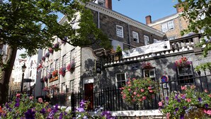 Un edificio histórico con muros de piedra, macetas con flores y una cerca de metal negro.